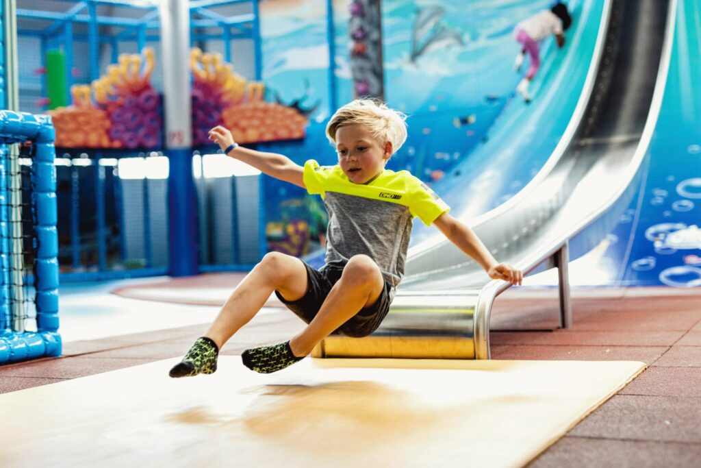 Junge fährt mit Spaß auf der großen Metallrutsche im Indoor-Spielplatz Playworld Wien